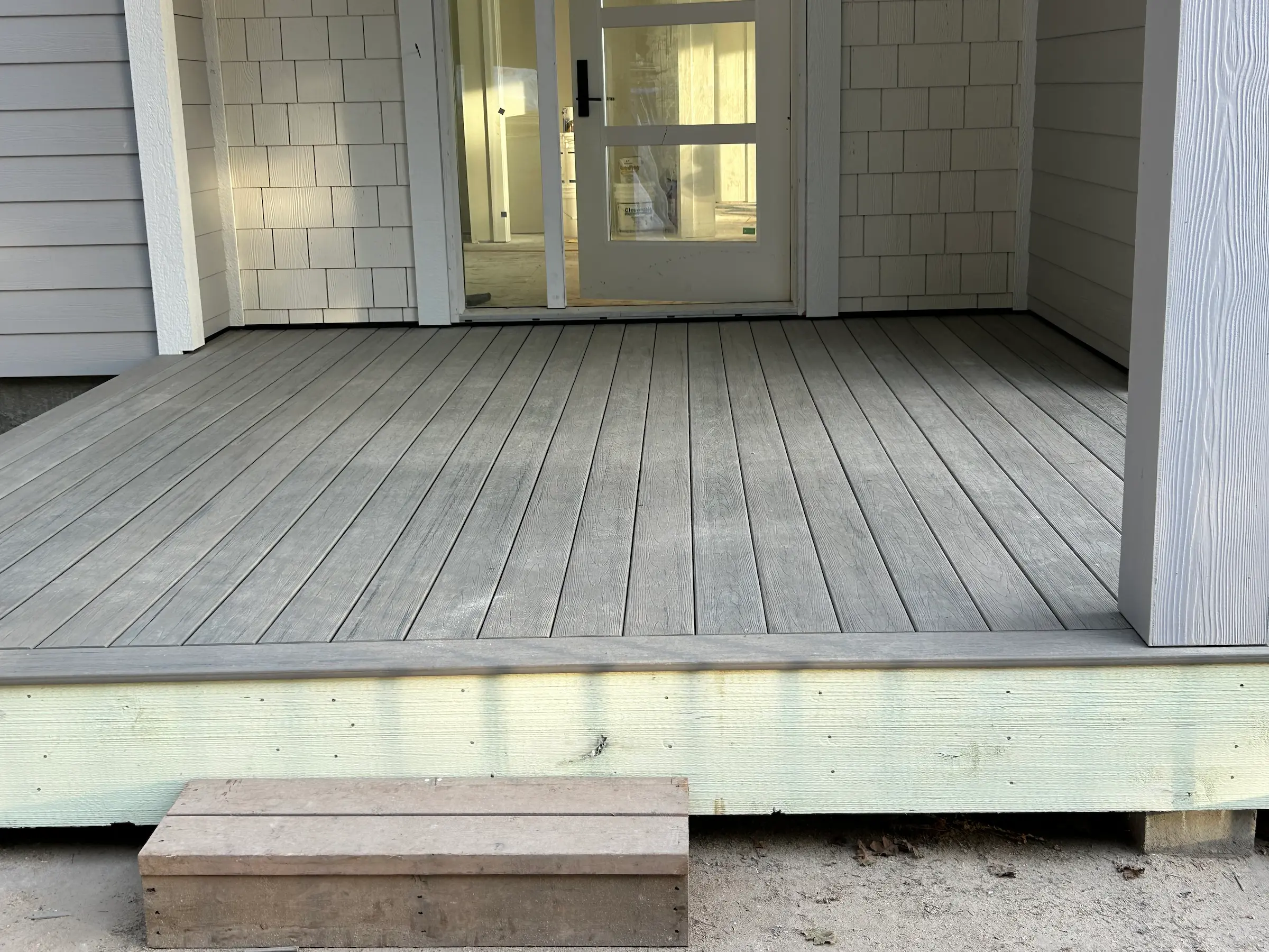A newly built wooden porch with a small step in front of a glass door.